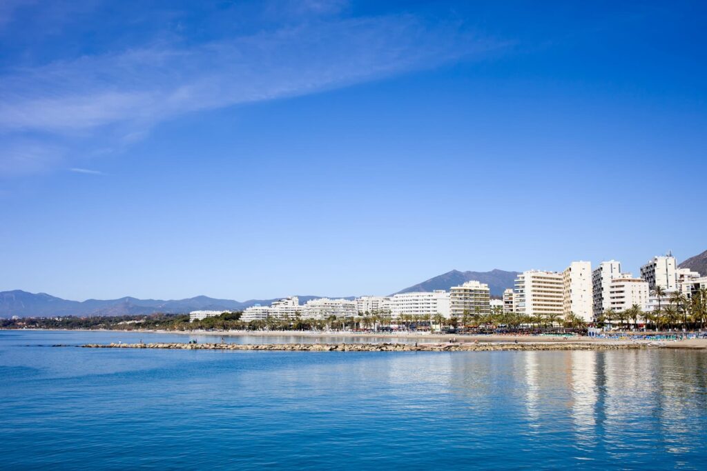 Panoramic view of Marbella’s coastline with calm blue sea, boats and La Concha mountain in the background – showcasing the Mediterranean lifestyle.